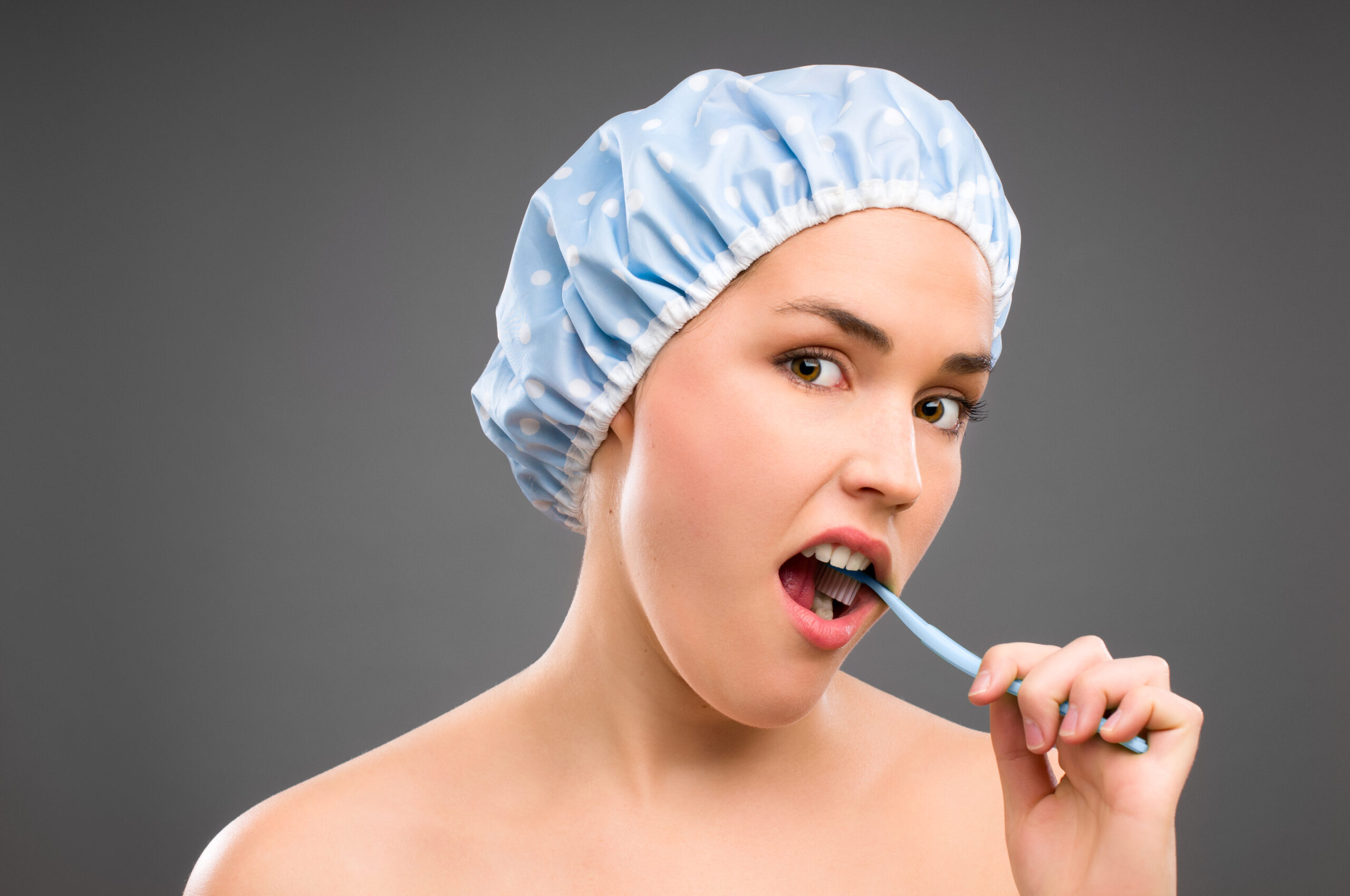 Woman brushing teeth wearing shower cap, illustrating daily oral hygiene for bleeding gums.