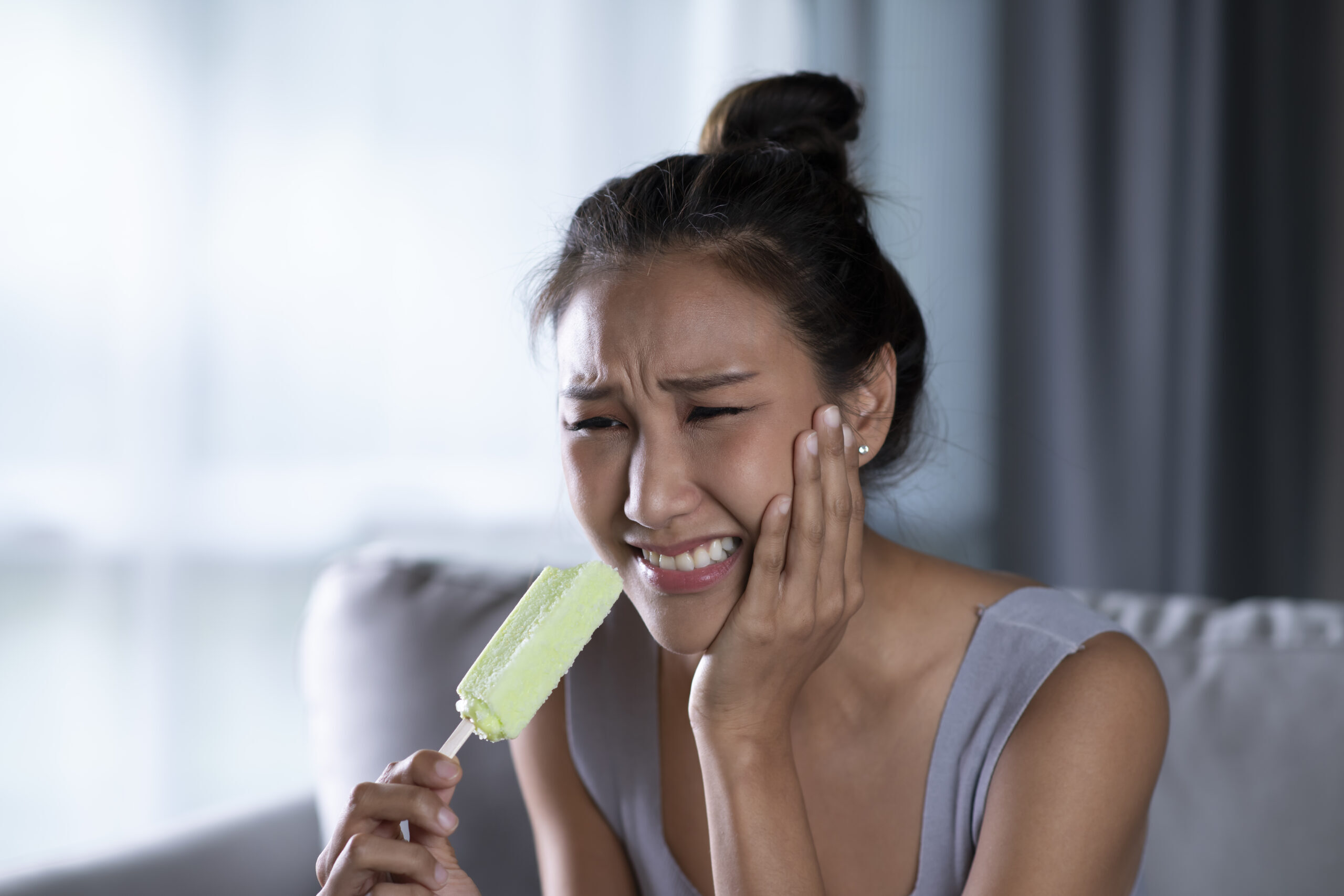 Woman experiencing tooth pain while holding a popsicle, illustrating dental sensitivity and emergency symptoms.