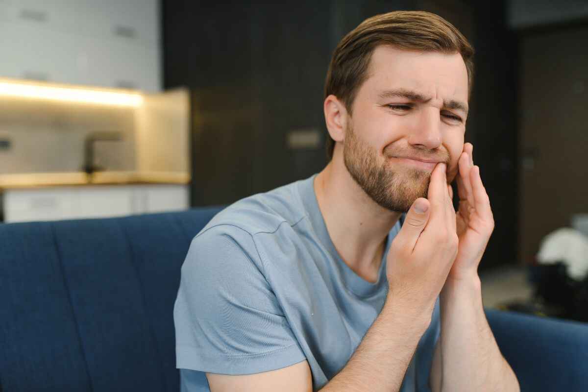 Man holding his cheek in pain from a throbbing toothache at home.