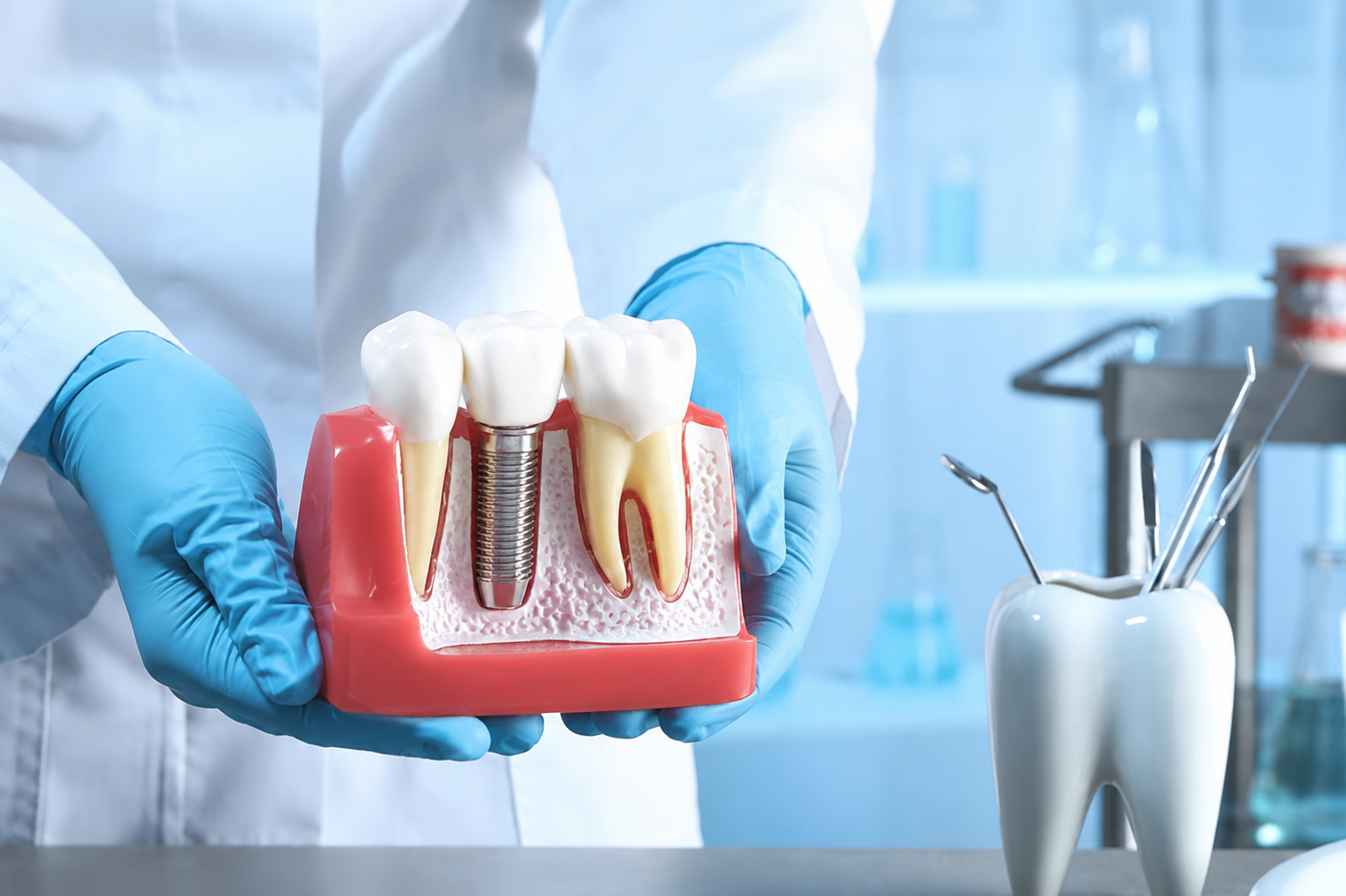 Dentist holding dental implant model showing tooth replacement procedure with crown and titanium post.